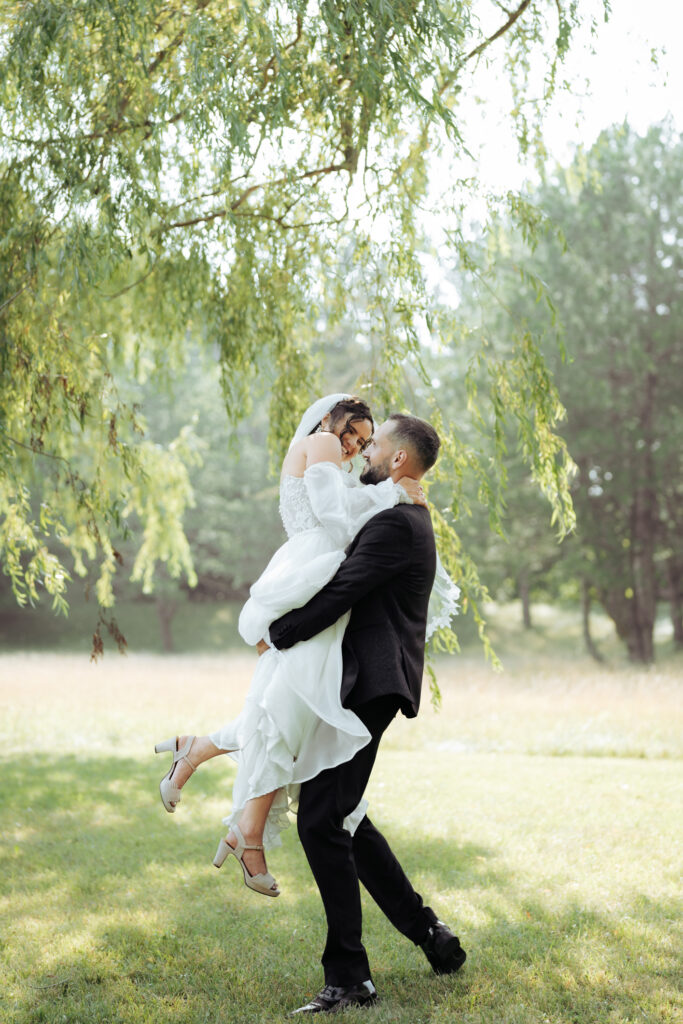 Romantic couple portrait in natural light with the bride’s veil flowing and horses grazing in the background.
