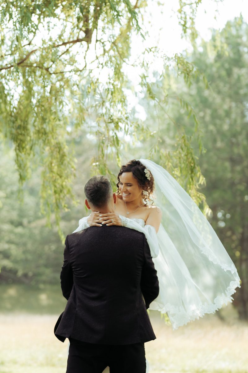 Romantic couple portrait in natural light with the bride’s veil flowing and horses grazing in the background.